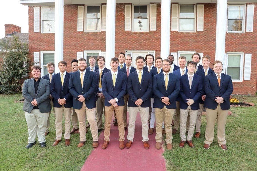 Men gathered around, posed in the front of the Pi Kappa Alpha house. 