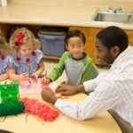 A man helps children sitting at a table.