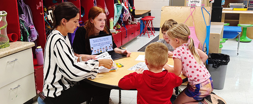 student teacher showing laptop with school material to children