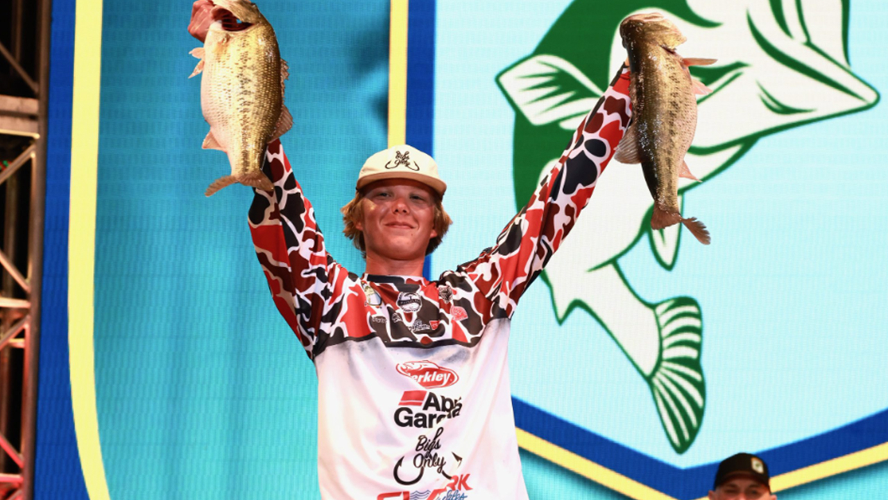 A young bass fisher from the UNA Bass Fishing Team holding two Bass Fish on a stage