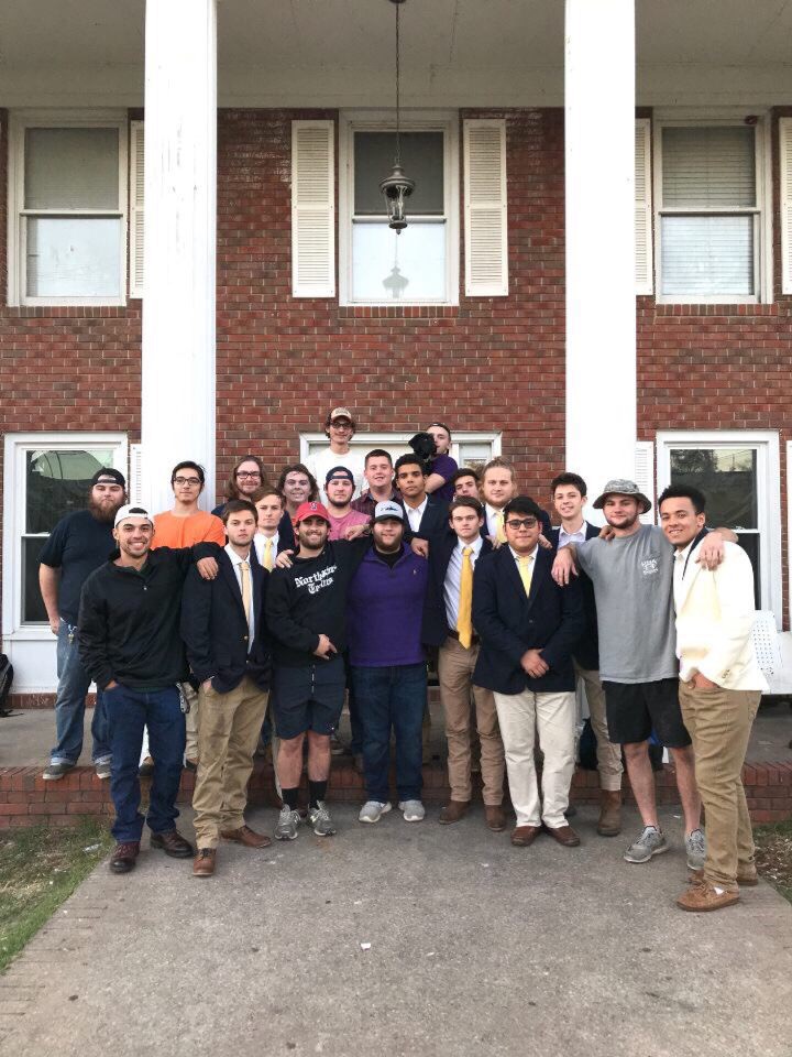 Men gathered around, posed in the front of the Pi Kappa Alpha house. 