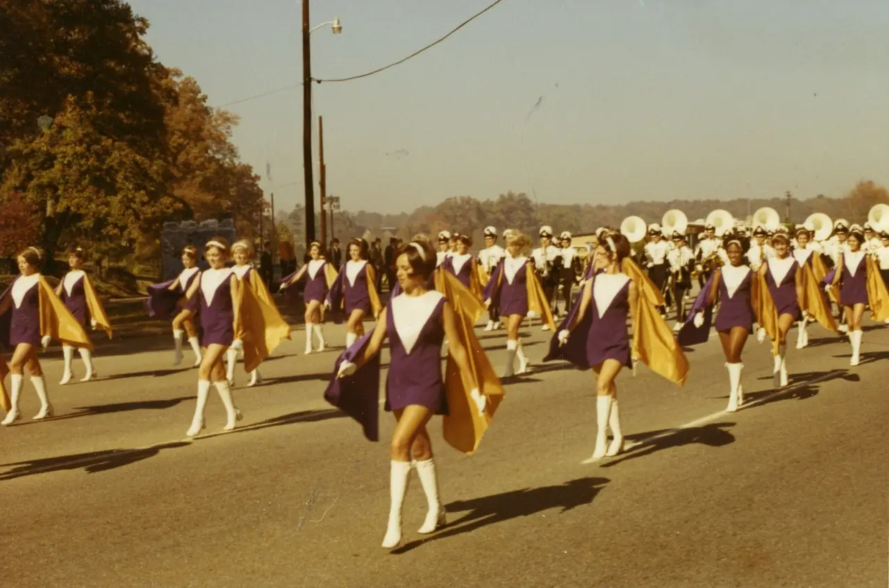 Majorettes in purple with gold capes leading the band down the street