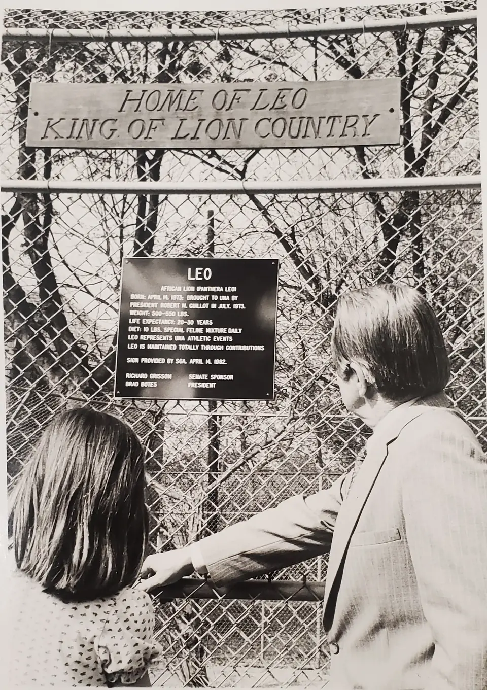 President Guillot and a child at the fence of Leo&rsquo;s enclosure, beneath signs reading Home of Leo, King of Lion Country