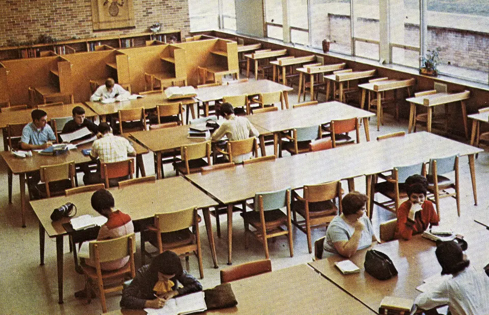 Students studying at long wooden tables in the library reading room