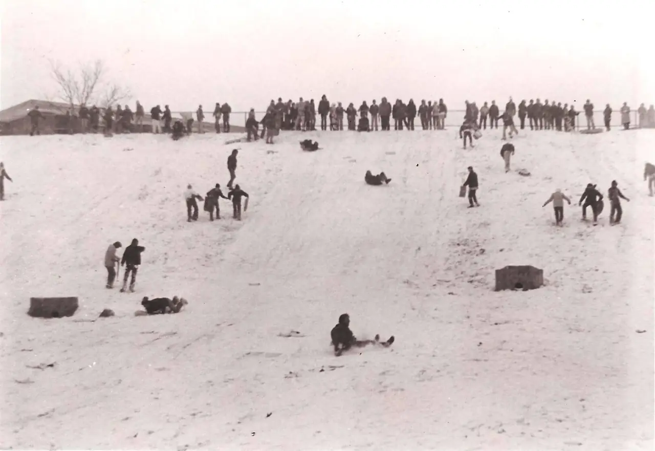 Students sledding down a snow-covered hill while a crowd watches from the top