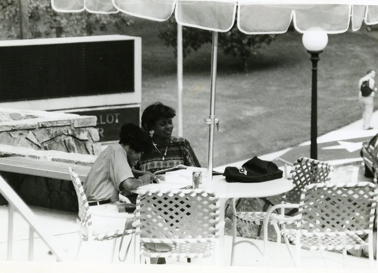 Two students talking at an umbrella table outside the Guillot University Center