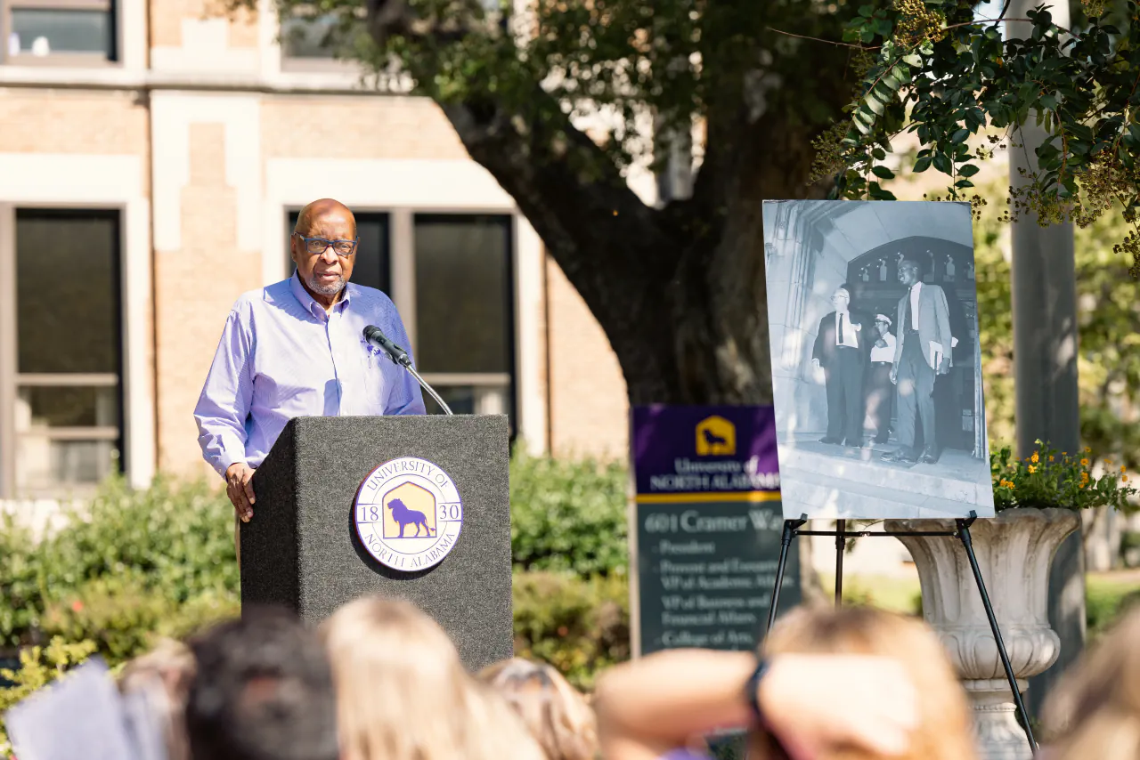 Wendell Gunn speaking at a lectern beside an easel holding an enlarged print of the 1963 photograph