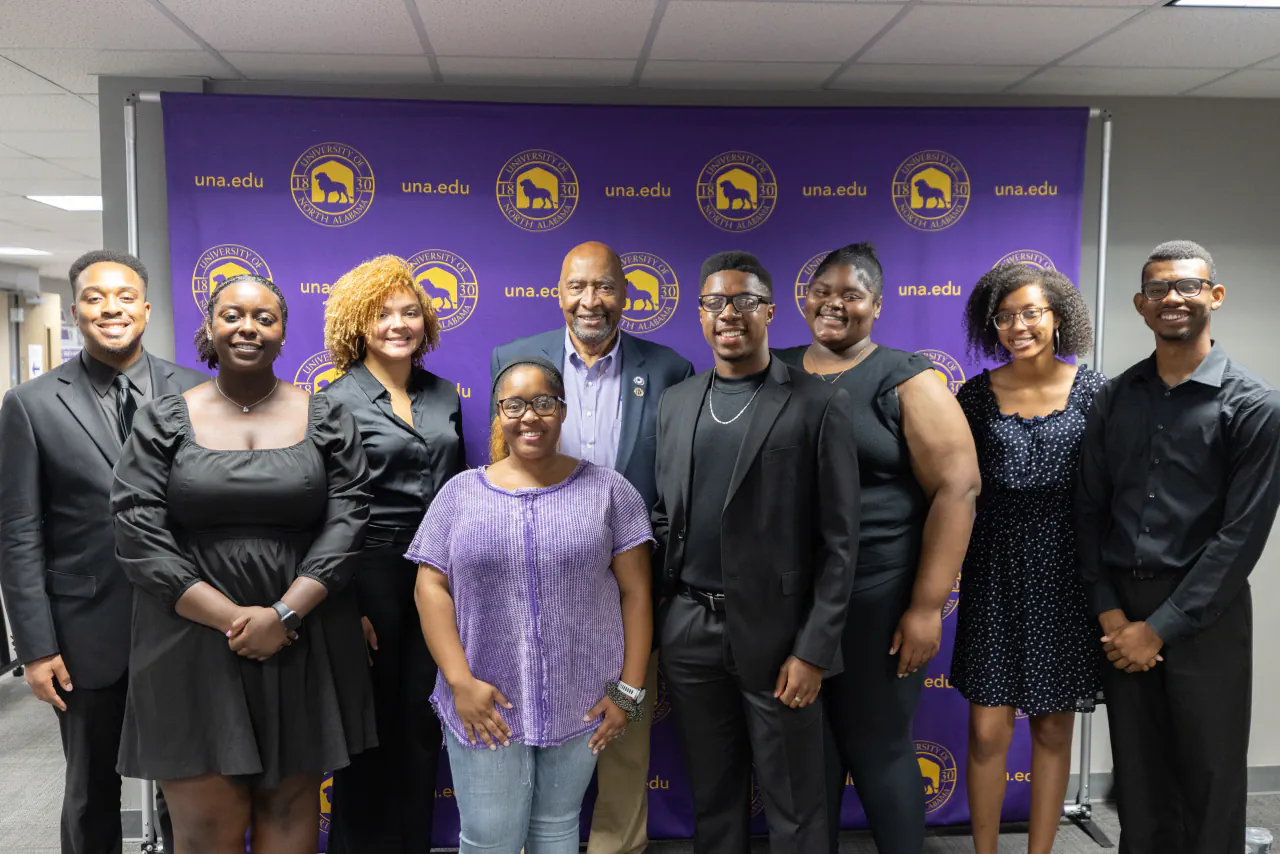 A group of students photographed together in front of a University of North Alabama backdrop